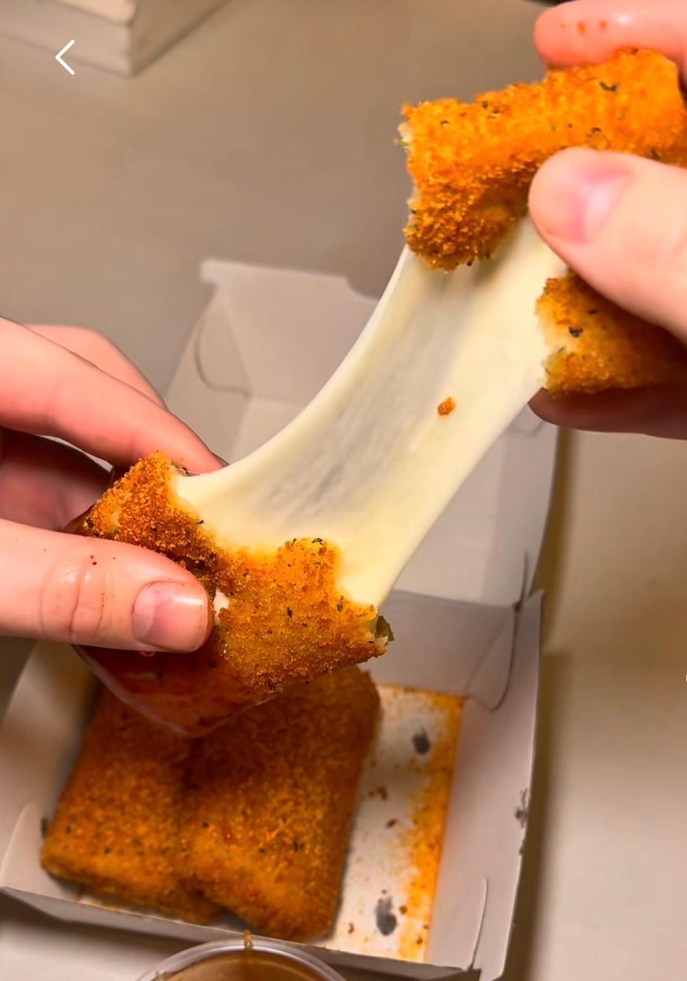 Crispy mozzarella stick being pulled apart with melted cheese stretching