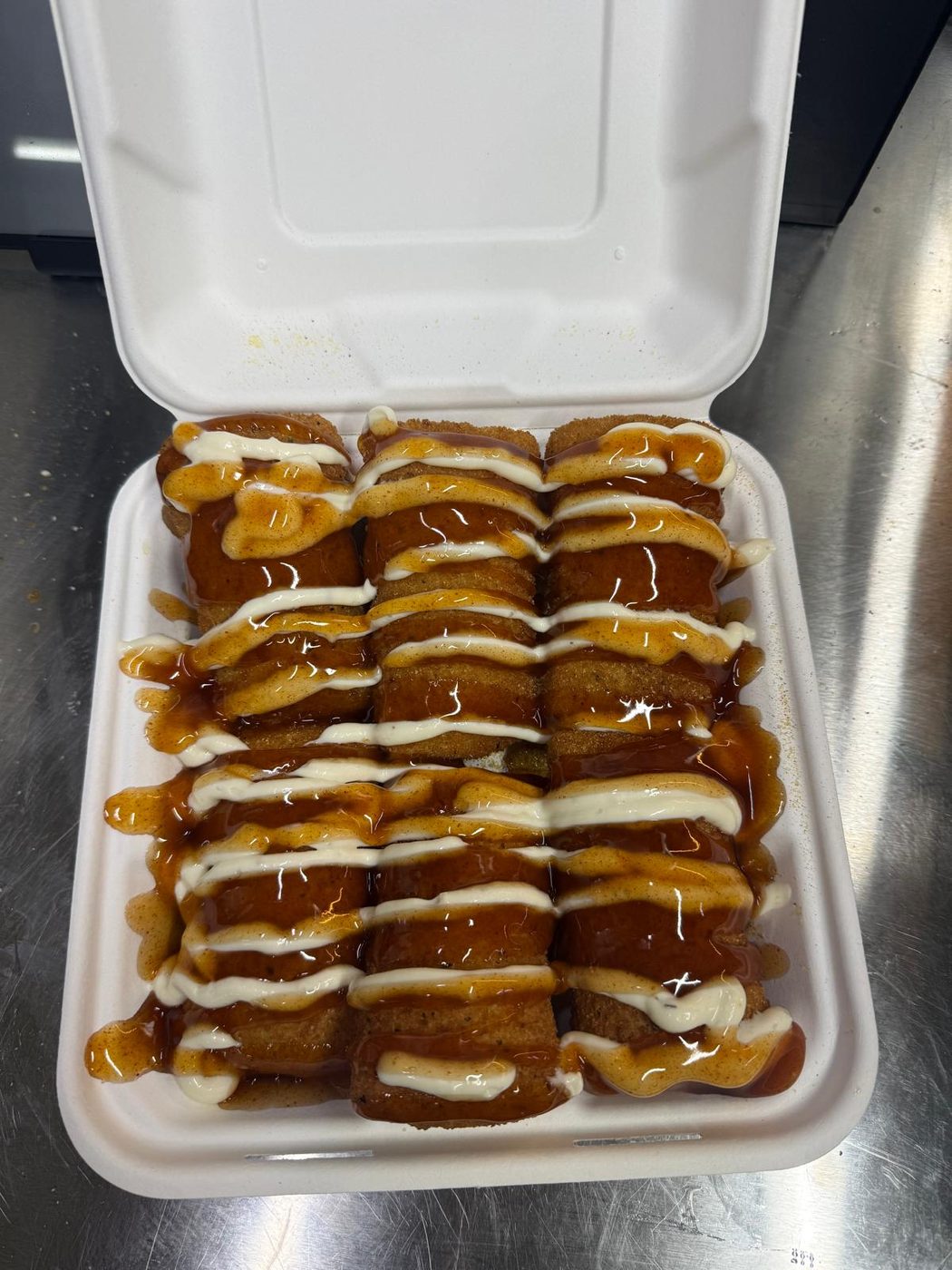 Crispy sticks loaded with sauce and mayo drizzle in a takeaway box
