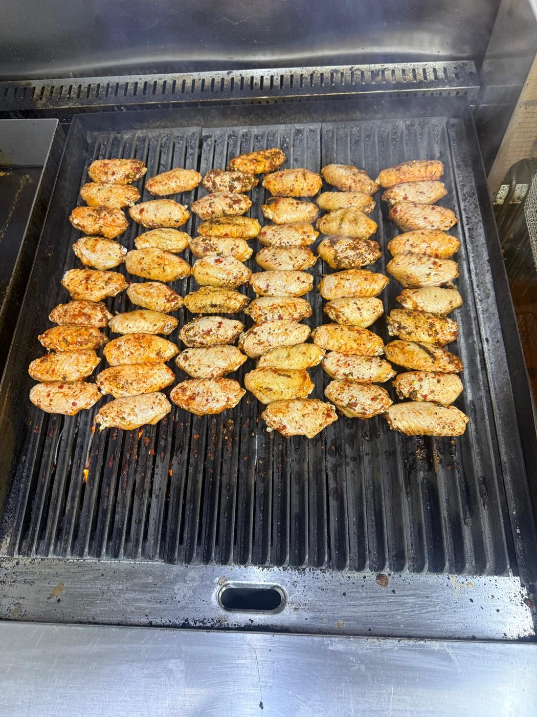 Rows of seasoned chicken wings cooking on the grill